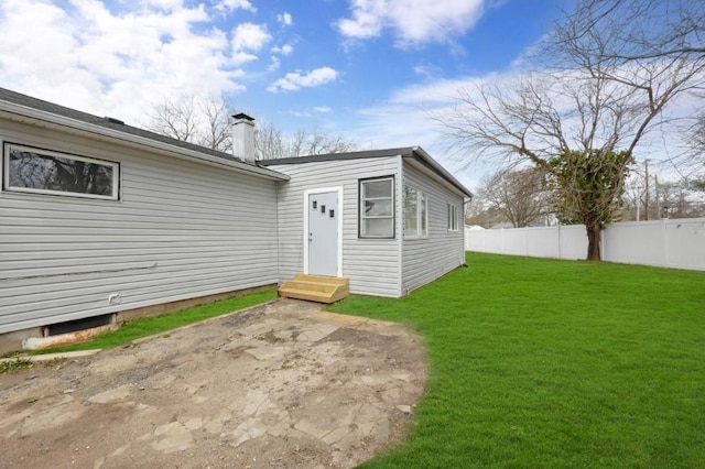 rear view of house featuring entry steps, a patio area, a yard, a chimney, and fence