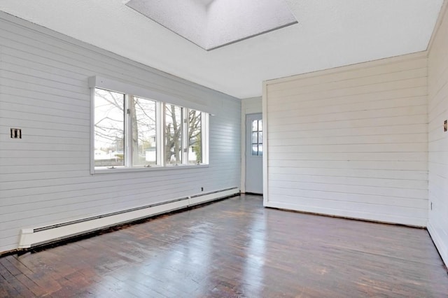 unfurnished room with wooden walls, a baseboard heating unit, and wood finished floors