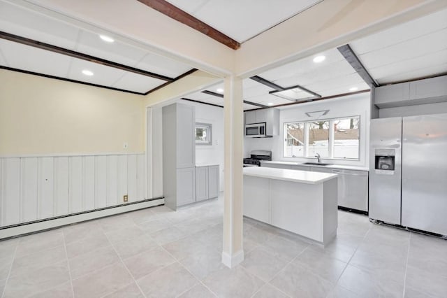 kitchen with a sink, light countertops, appliances with stainless steel finishes, a wainscoted wall, and a baseboard heating unit