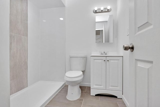 bathroom with baseboards, toilet, vanity, tile patterned floors, and tiled shower