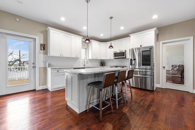 kitchen with light countertops, white cabinetry, a kitchen island, decorative backsplash, and appliances with stainless steel finishes