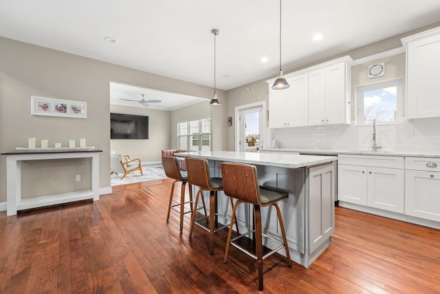 kitchen with a center island, white cabinets, a sink, dark wood-style flooring, and a breakfast bar area