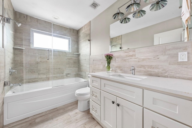 bathroom with visible vents, combined bath / shower with glass door, toilet, tile walls, and vanity