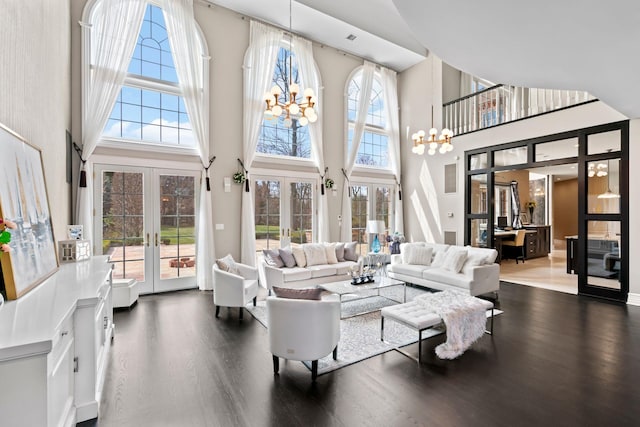 living area featuring french doors, wood finished floors, a towering ceiling, and a notable chandelier