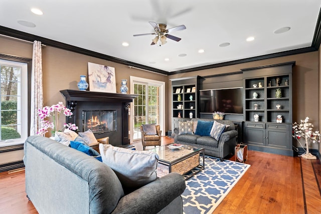 living room featuring a glass covered fireplace, recessed lighting, crown molding, a ceiling fan, and wood finished floors