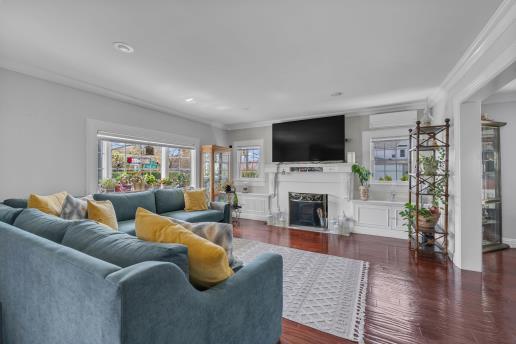 living area featuring a fireplace with flush hearth, wood finished floors, and ornamental molding