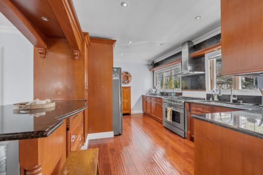 kitchen featuring brown cabinets, stainless steel appliances, dark stone countertops, wood finished floors, and wall chimney range hood