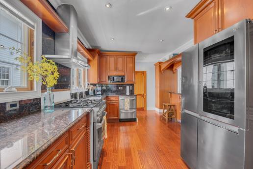 kitchen with light wood finished floors, brown cabinetry, stone counters, and appliances with stainless steel finishes