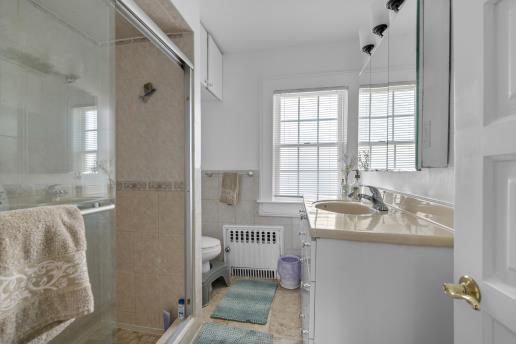 bathroom featuring radiator, toilet, vanity, tile walls, and a stall shower