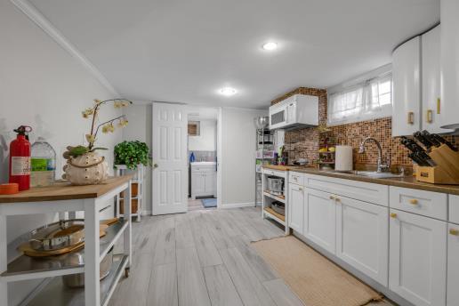 kitchen with backsplash, light wood-type flooring, white cabinetry, and a sink