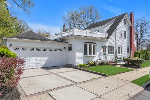 view of front facade featuring an attached garage, a chimney, a balcony, and driveway