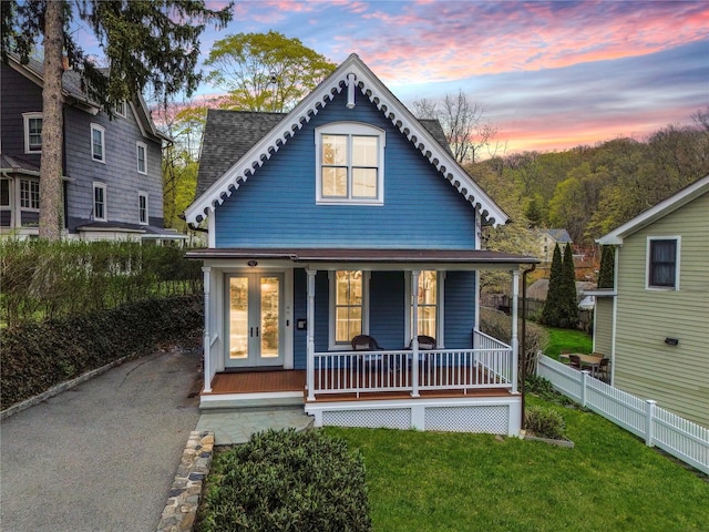 view of front of house with fence, covered porch, a shingled roof, and a yard