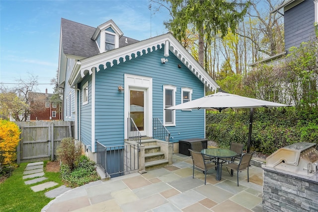 rear view of property with fence, a patio, roof with shingles, an outdoor kitchen, and entry steps