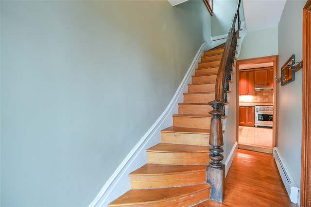 stairway with wood finished floors and a baseboard heating unit