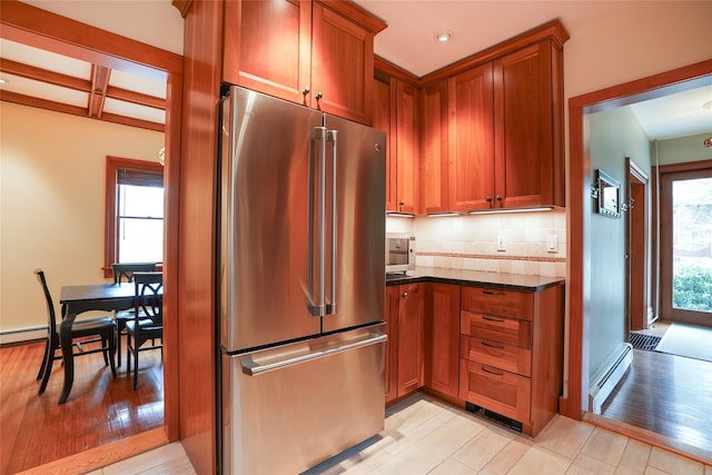 kitchen with brown cabinetry, tasteful backsplash, freestanding refrigerator, dark stone countertops, and recessed lighting