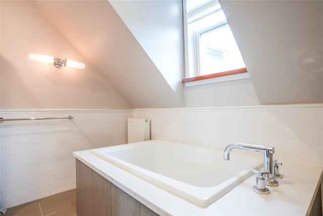 full bathroom with a garden tub, a sink, wainscoting, and tile walls