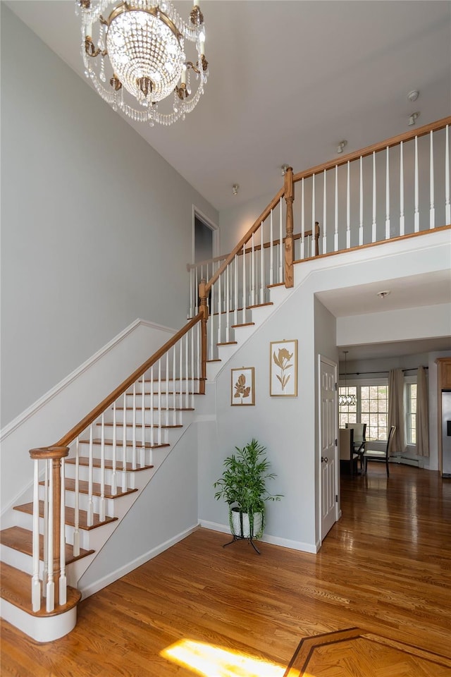 stairs featuring a high ceiling, baseboards, an inviting chandelier, and wood finished floors