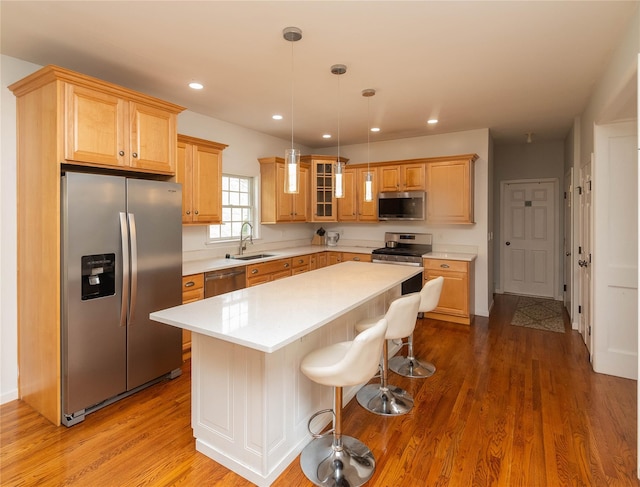 kitchen featuring a kitchen island, wood finished floors, light countertops, a sink, and stainless steel appliances