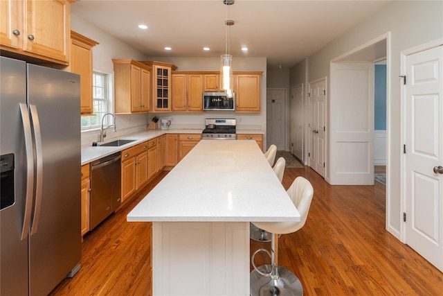 kitchen with glass insert cabinets, a kitchen island, wood finished floors, a sink, and stainless steel appliances