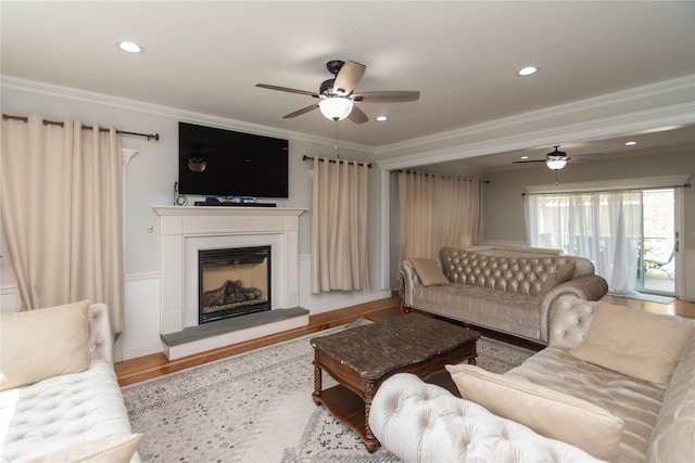 living area featuring crown molding, ceiling fan, wood finished floors, and a glass covered fireplace