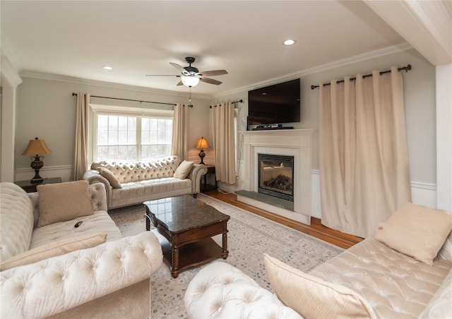 living room with crown molding, a ceiling fan, a glass covered fireplace, recessed lighting, and wood finished floors