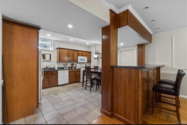 kitchen featuring recessed lighting, white appliances, dark countertops, a breakfast bar area, and brown cabinetry