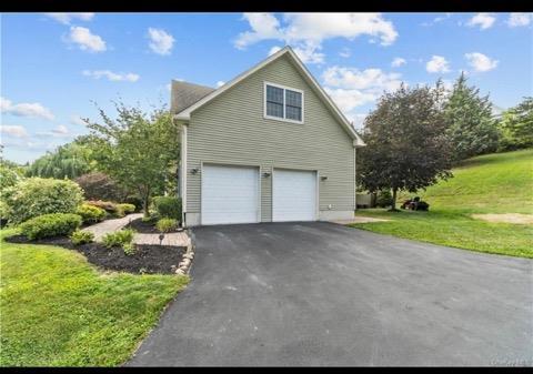 view of side of home with a garage, aphalt driveway, and a lawn