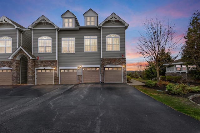 view of property with an attached garage, driveway, and stone siding