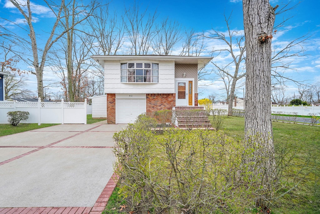 42 The Blvd, North Amityville, NY 11701 - raised ranch with concrete driveway, a front lawn, brick siding, a garage, and fence