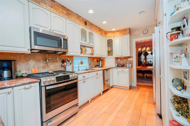 kitchen featuring tasteful backsplash, glass insert cabinets, a sink, stainless steel appliances, and light stone counters