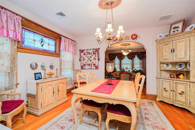 dining area with arched walkways, light wood finished floors, a notable chandelier, and visible vents
