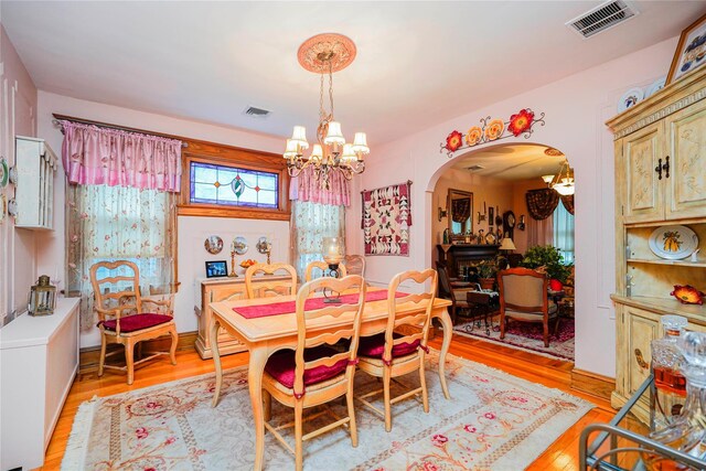dining space featuring visible vents, light wood-type flooring, arched walkways, and an inviting chandelier