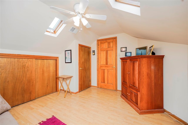 additional living space with visible vents, baseboards, a ceiling fan, lofted ceiling with skylight, and light wood-style flooring