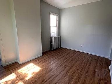 spare room with baseboards, radiator, and wood finished floors
