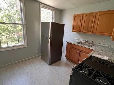 kitchen with brown cabinetry, black appliances, light stone counters, a sink, and light wood finished floors