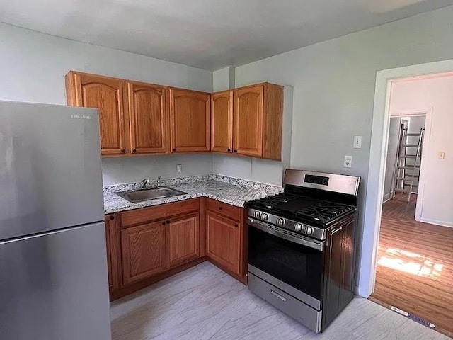kitchen featuring a sink, light wood-style flooring, appliances with stainless steel finishes, and brown cabinets