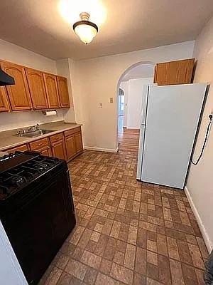 kitchen with black range with gas cooktop, arched walkways, a sink, freestanding refrigerator, and brown cabinetry