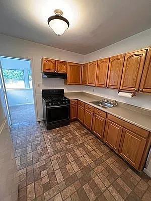 kitchen featuring brown cabinetry, gas stove, brick patterned floor, and under cabinet range hood