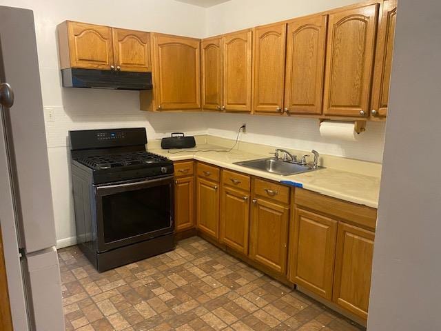 kitchen with freestanding refrigerator, under cabinet range hood, gas stove, light countertops, and a sink
