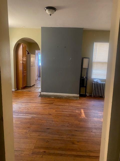 empty room featuring arched walkways, radiator, and light wood finished floors