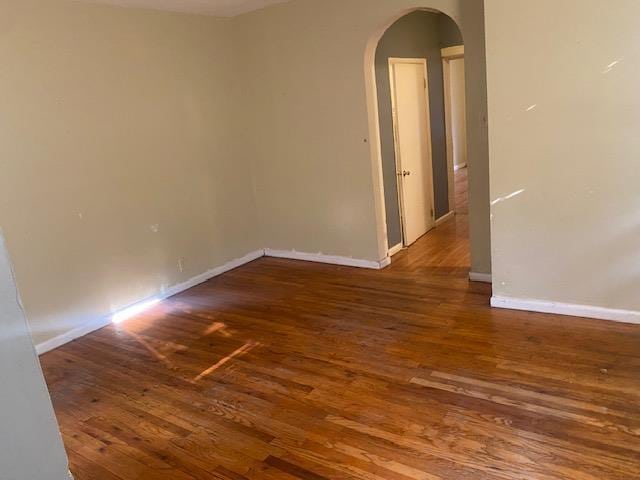 unfurnished room featuring baseboards, arched walkways, and wood finished floors