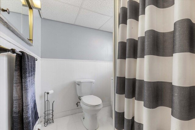 bathroom featuring tile patterned floors, a drop ceiling, a wainscoted wall, toilet, and a shower with shower curtain