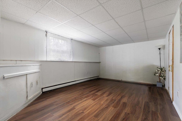 basement featuring baseboard heating, baseboards, wood finished floors, and a paneled ceiling