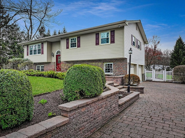 bi-level home with an attached garage, fence, and decorative driveway