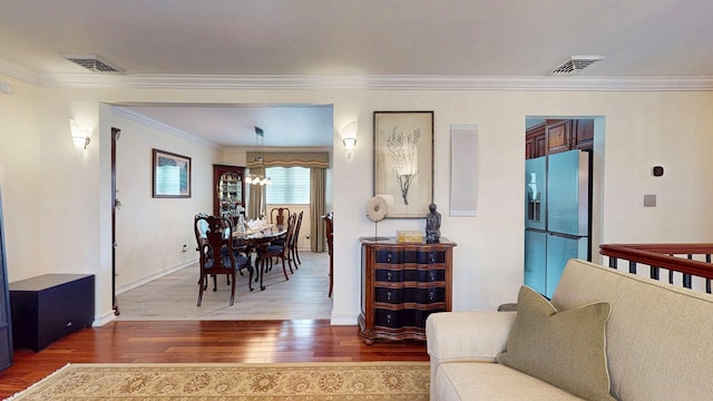 living room with baseboards, a chandelier, crown molding, visible vents, and hardwood / wood-style floors
