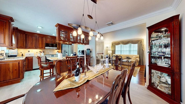 dining area with ornamental molding, visible vents, and light wood-style flooring