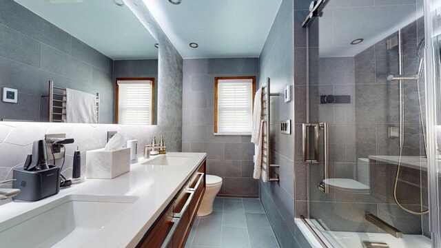 bathroom featuring a sink, tile walls, toilet, tile patterned flooring, and a stall shower