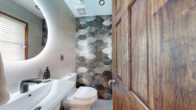 bathroom with tile walls, a sink, and toilet