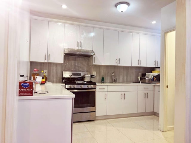 kitchen with under cabinet range hood, light countertops, backsplash, stainless steel range with gas cooktop, and white cabinetry
