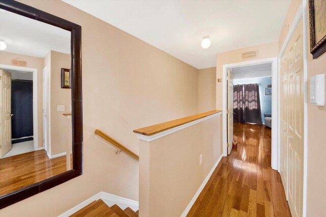 hallway featuring baseboards, wood finished floors, and an upstairs landing